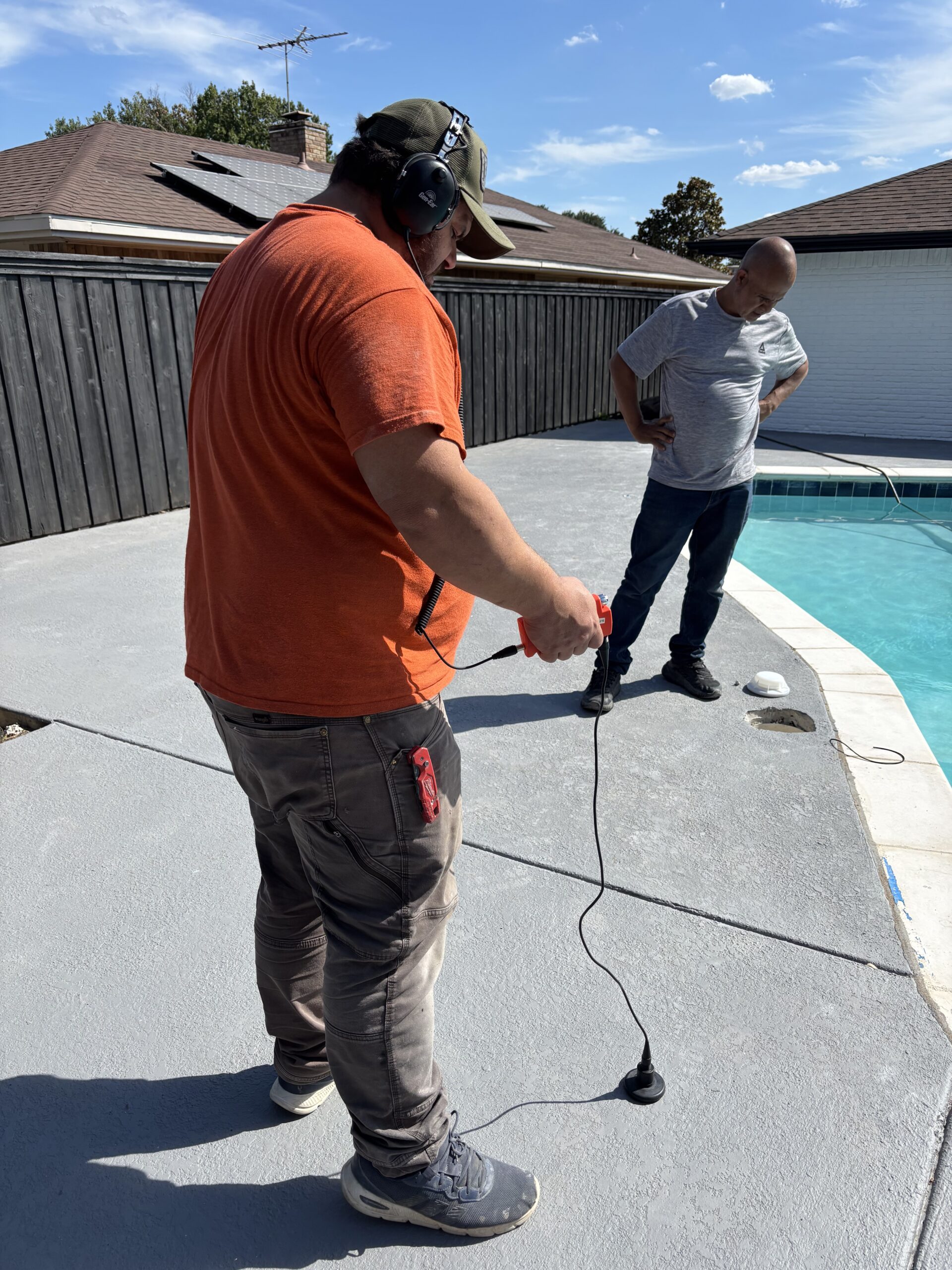 Pool leak detection technician using electronic listening equipment on a residential pool deck